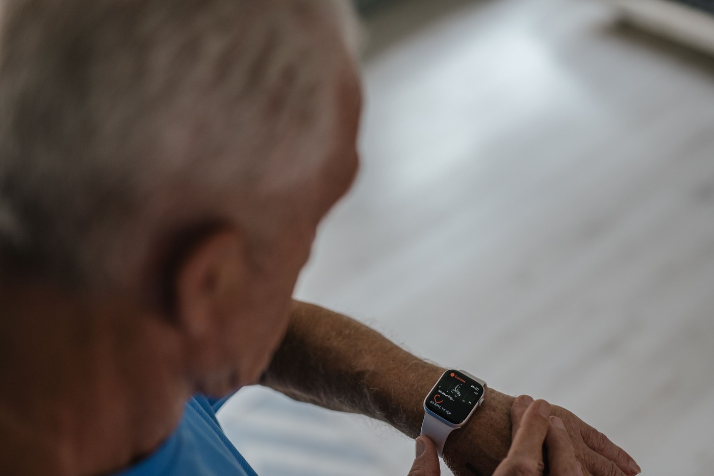An older man checks the smartwatch on his wrist at home.